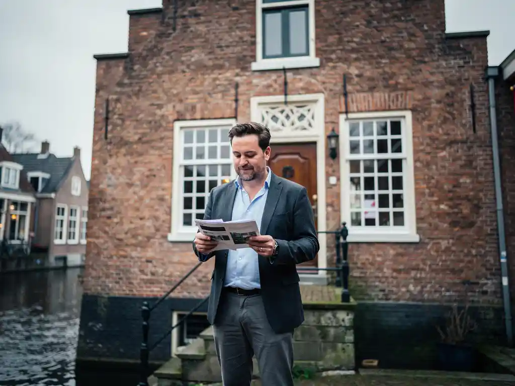 Makelaar met property documenten voor een 17e-eeuws Gouds grachtenpand met rode trapgevel en roedenverdeling ramen.