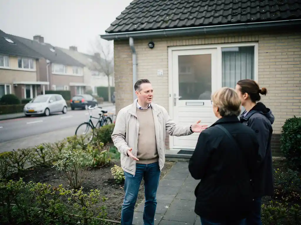 Makelaar bespreekt jaren '80 twee-onder-een-kapwoning in Waddinxveen met geïnteresseerd stel bij de voordeur.
