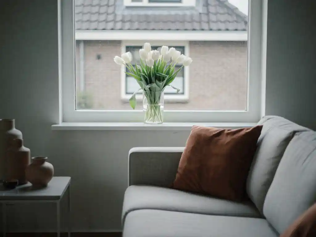 Witte tulpen op een schone vensterbank in een opgeruimde woonkamer in Waddinxveen, met lichtgrijze bank en zicht op bakstenen gevel.