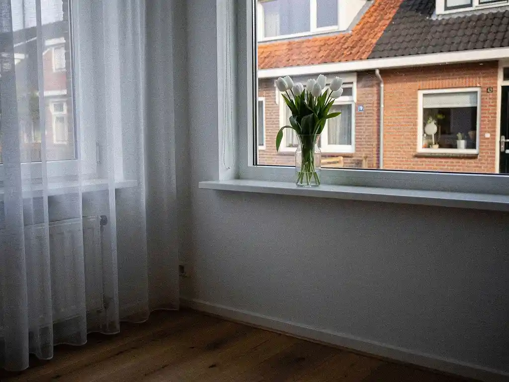 Woonkamerhoek in Bodegraven met witte tulpen op vensterbank, grijswitte muren, houten accenten en rode bakstenen gevel buiten.